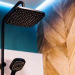 Black rain shower head and hand shower, with LED lighting on the ceiling in bathroom, close up.