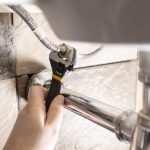 plumber hand fixes flexible hoses under sink by adjustable wrench closeup at home
